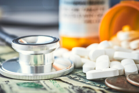 Pill bottles next to stethoscope and money