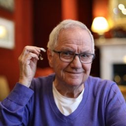 Senior man about to insert his hearing aid while wearing glasses