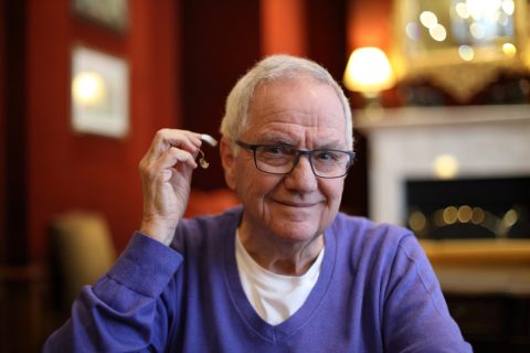 Senior man about to insert his hearing aid while wearing glasses