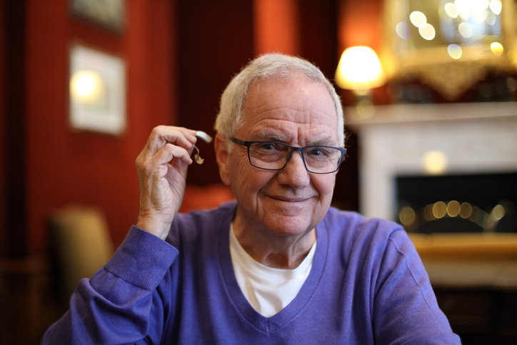 Senior man about to insert his hearing aid while wearing glasses