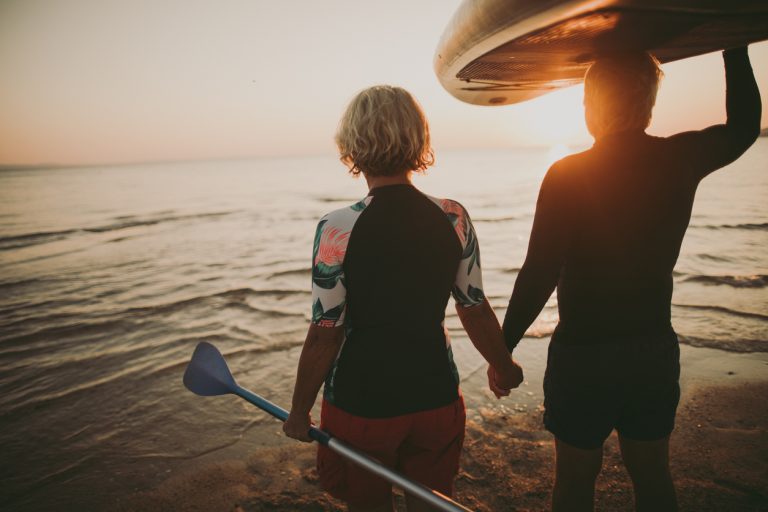an active senior couple heads into the ocean for a kayaking adventure