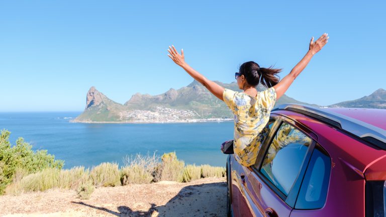 Woman outside a car window with hands up at Chapmans Peak Drive in Cape Town, South Africa