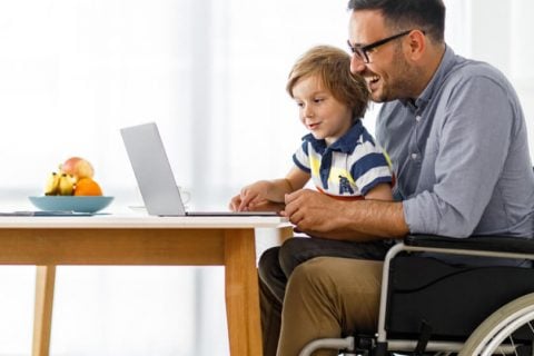 Man in wheelchair on laptop with his son in his lap