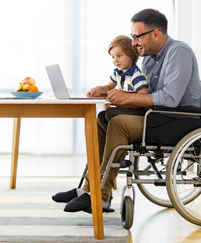 Man in wheelchair on laptop with his son in his lap