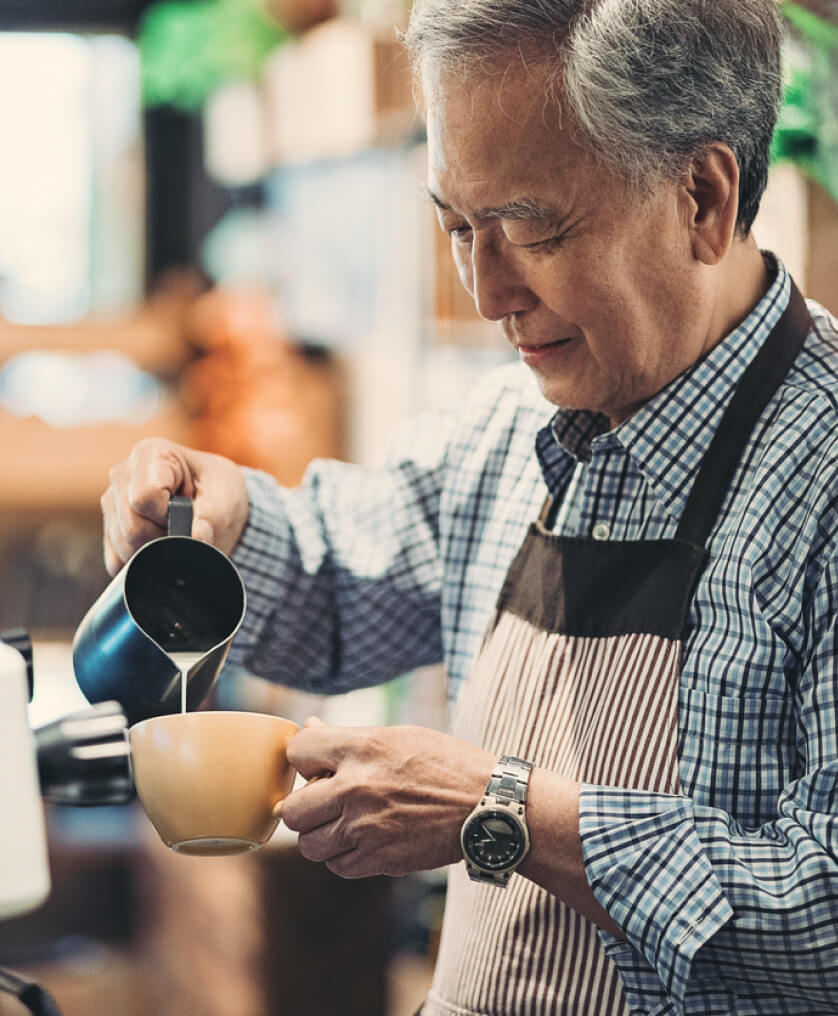 Elderly man pouring cream into a coffee cup