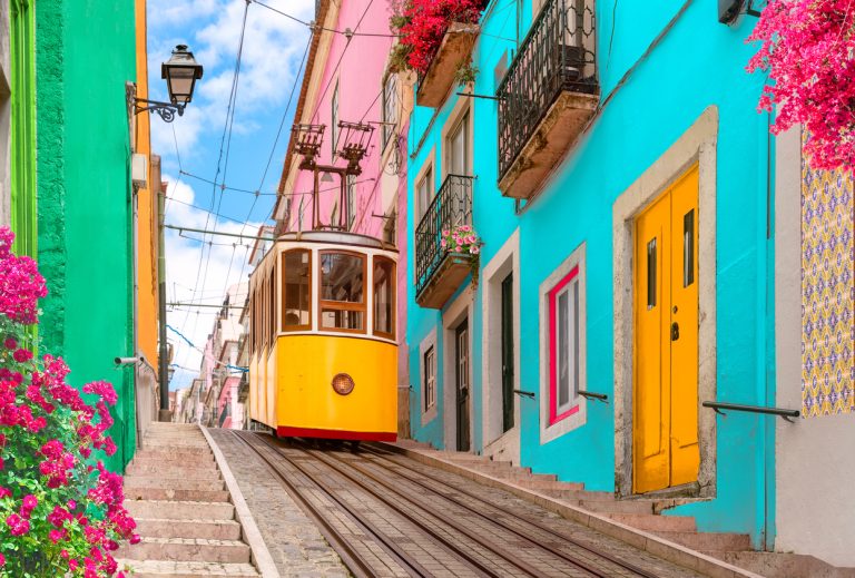 A yellow tram passes by colorfully painted homes in Libson, Portugal
