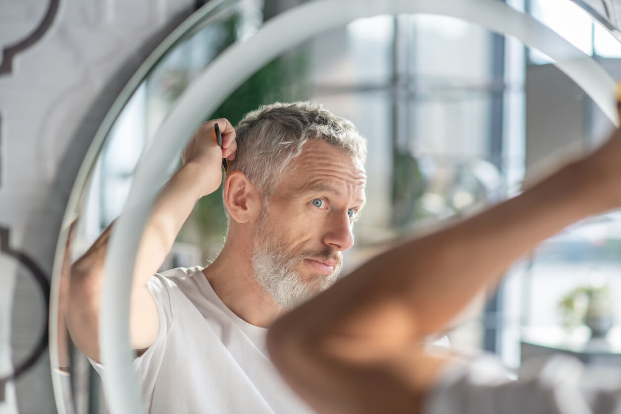 Man combing his grey hair in the mirror in the morning