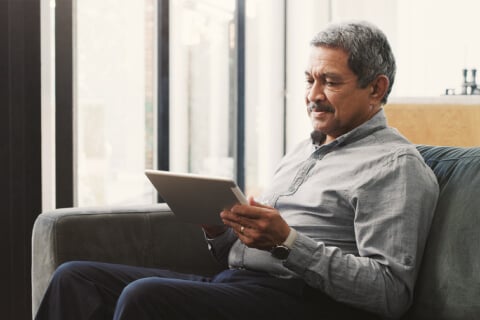 Elderly man sitting on couch using tablet