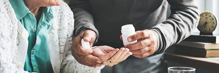 older man offering older woman medication