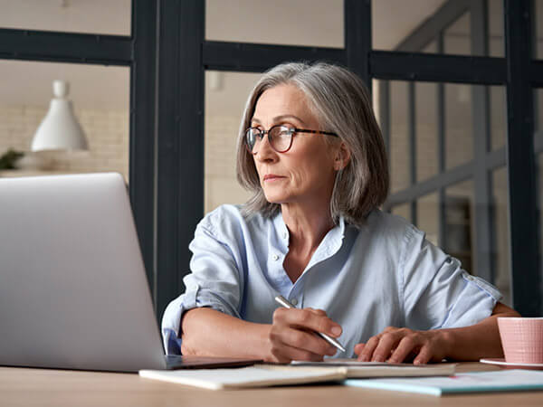 Older woman looking at laptop and taking notes