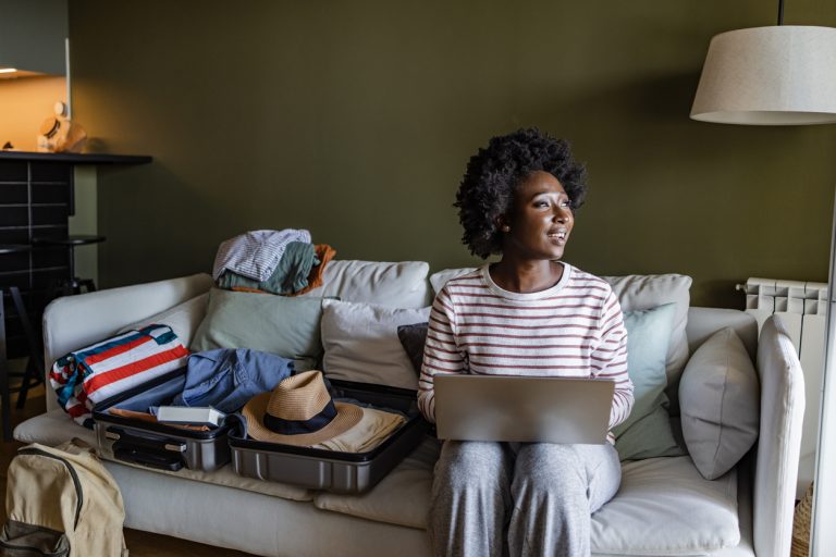 A woman plans her vacation online while packing her suitcase