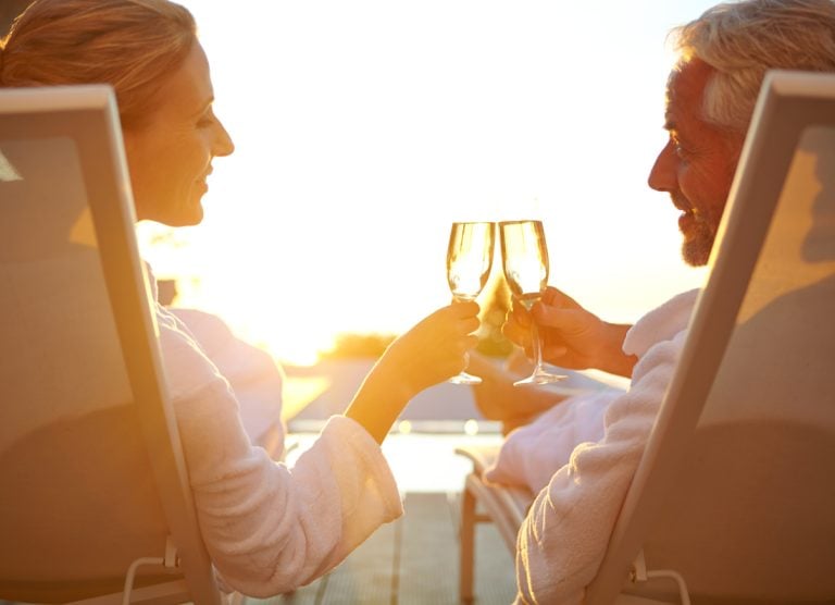 Rearview shot of a mature couple drinking champagne while relaxing in deck chairs at sunset