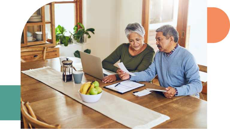 Photo of a retired couple discussing their household budget at the kitchen table with a laptop and papers