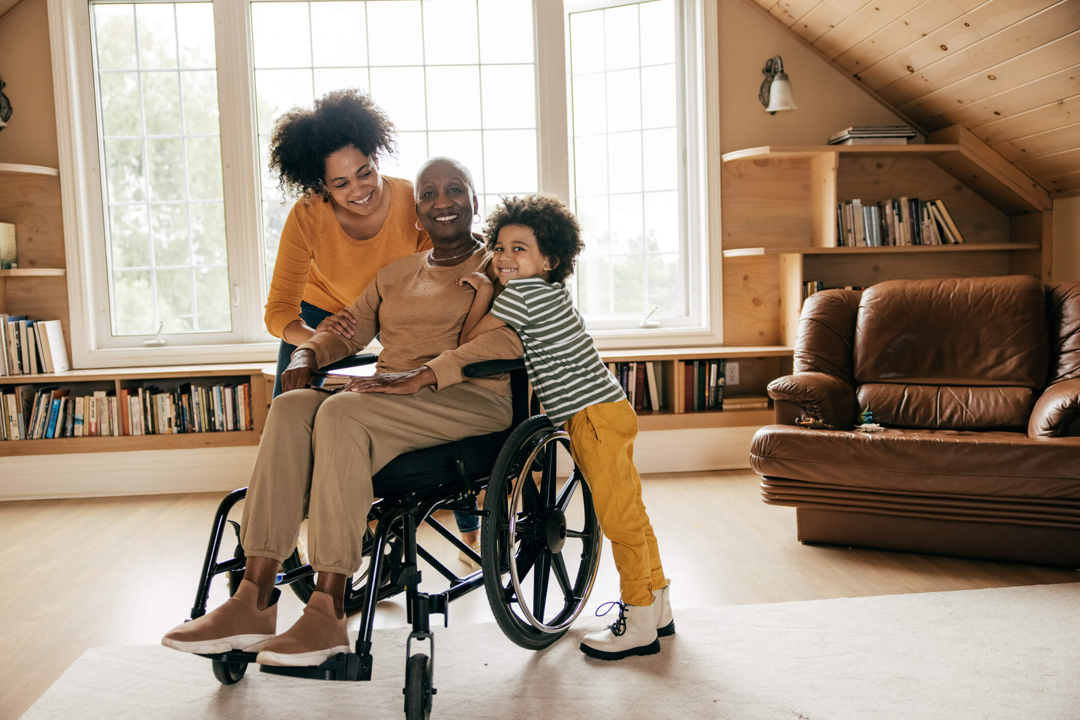 Woman in wheelchair smiling with her adult daughter and grandchild.