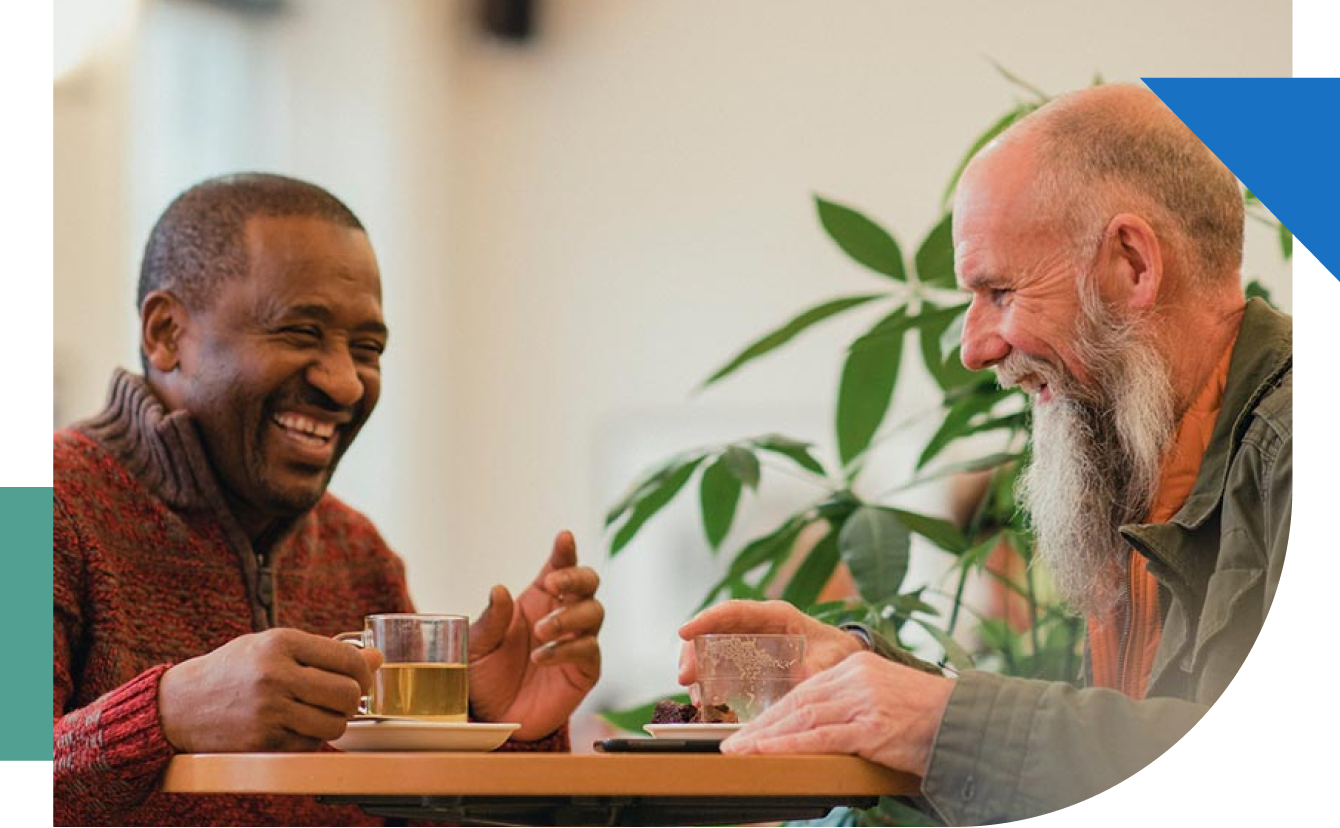 Candid photo of two senior men laughing while drinking tea.
